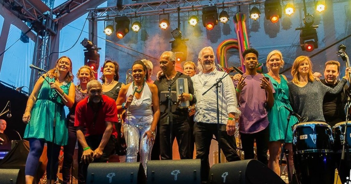 Groep muzikanten op het podium tijdens een optreden, met microfoons en instrumenten.