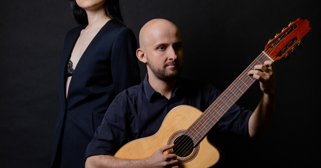 Een vrouw staat achter een man met een gitaar.