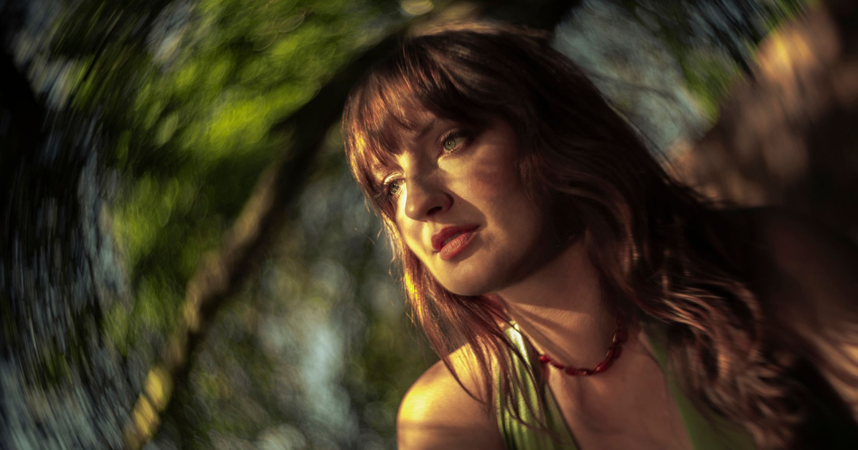 Portret van singer songwriter Madison Cunningham. Ze staat bij een boom en het zonlicht valt op haar gezicht