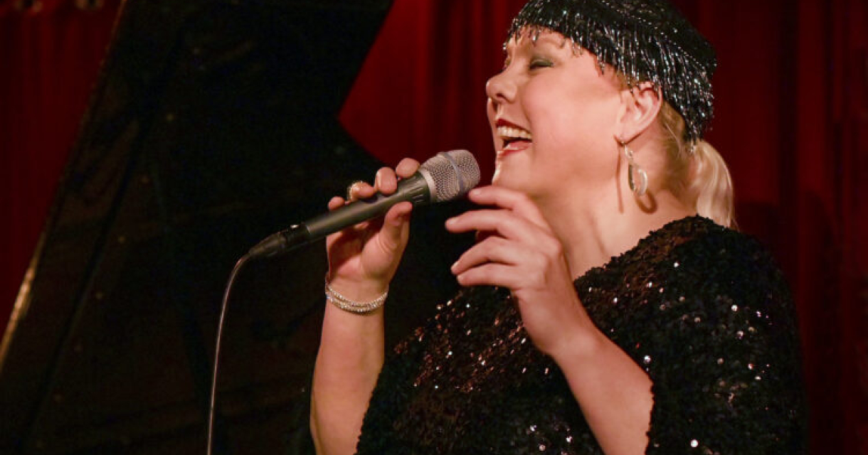 Female singer with a microphone and sparkling outfit sings enthusiastically.