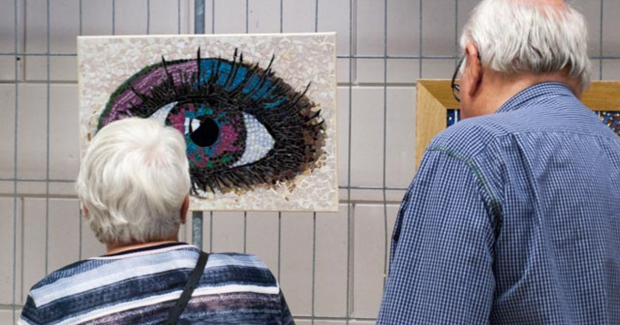 Twee oudere mensen kijken naar een kleurrijke mozaïek van een oog.