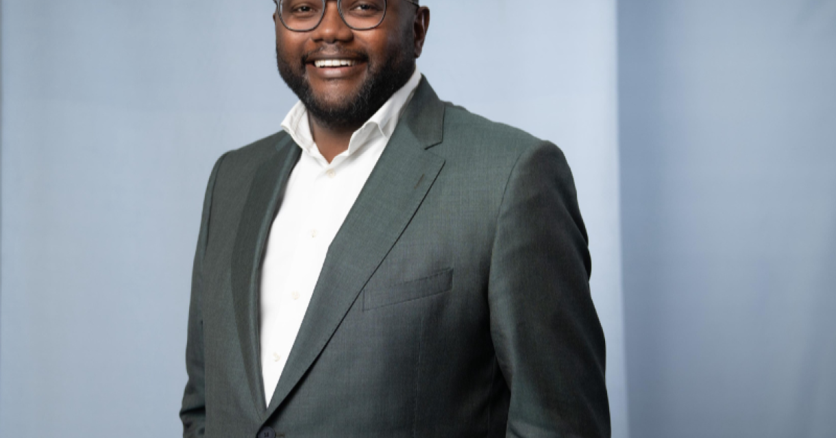 Man met bril, lachend in een groene blazer.