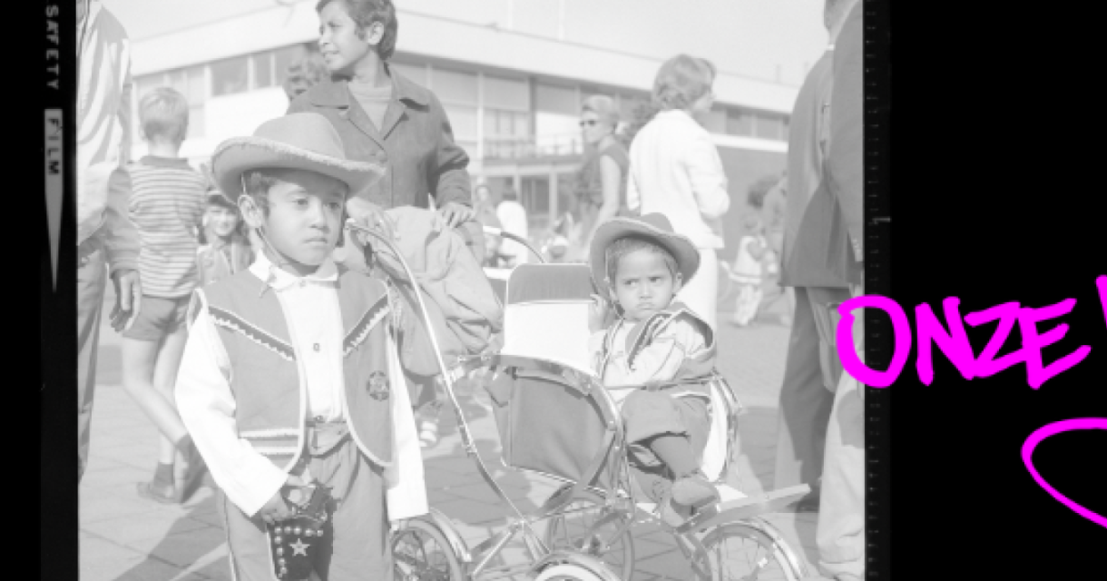 Een jongen en een meisje in traditionele kleding, met een kinderwagen op een druk plein.