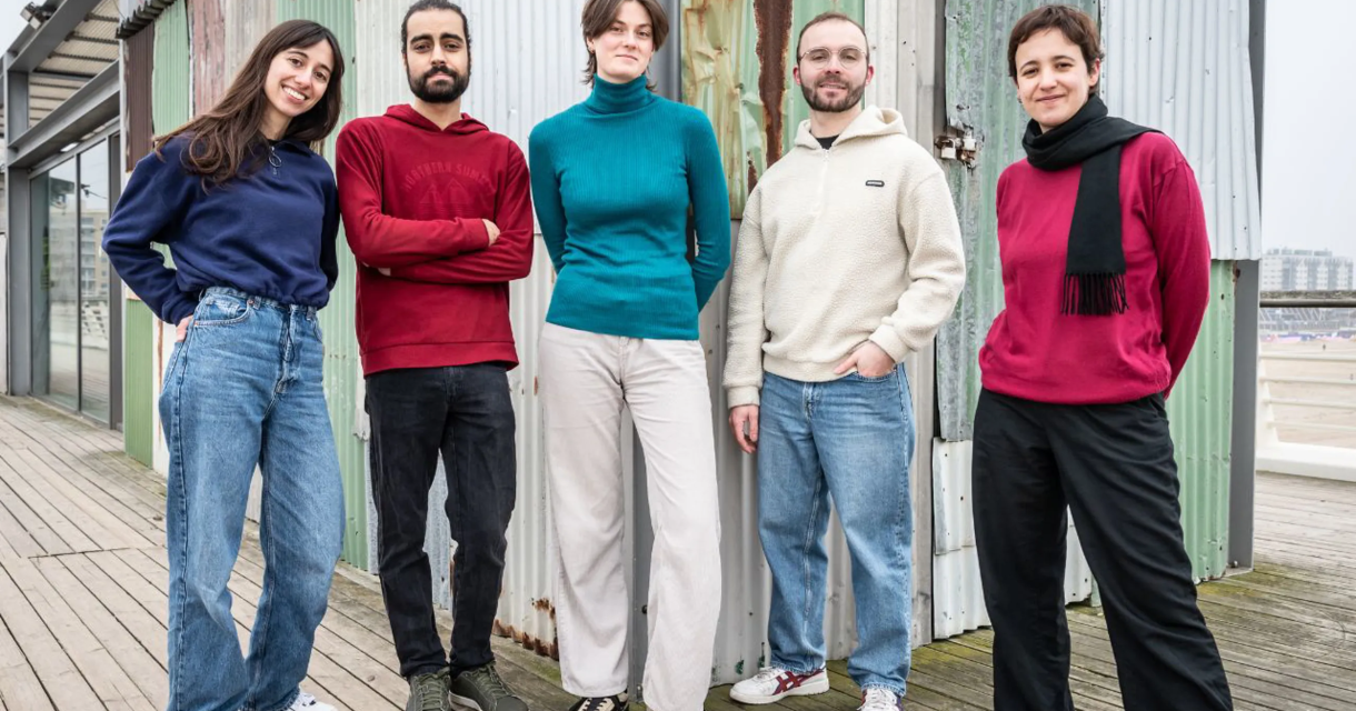 Vijf leden van Sketch351 staan op een houten vloer, voor een metalen achtergrond, in Den Haag.