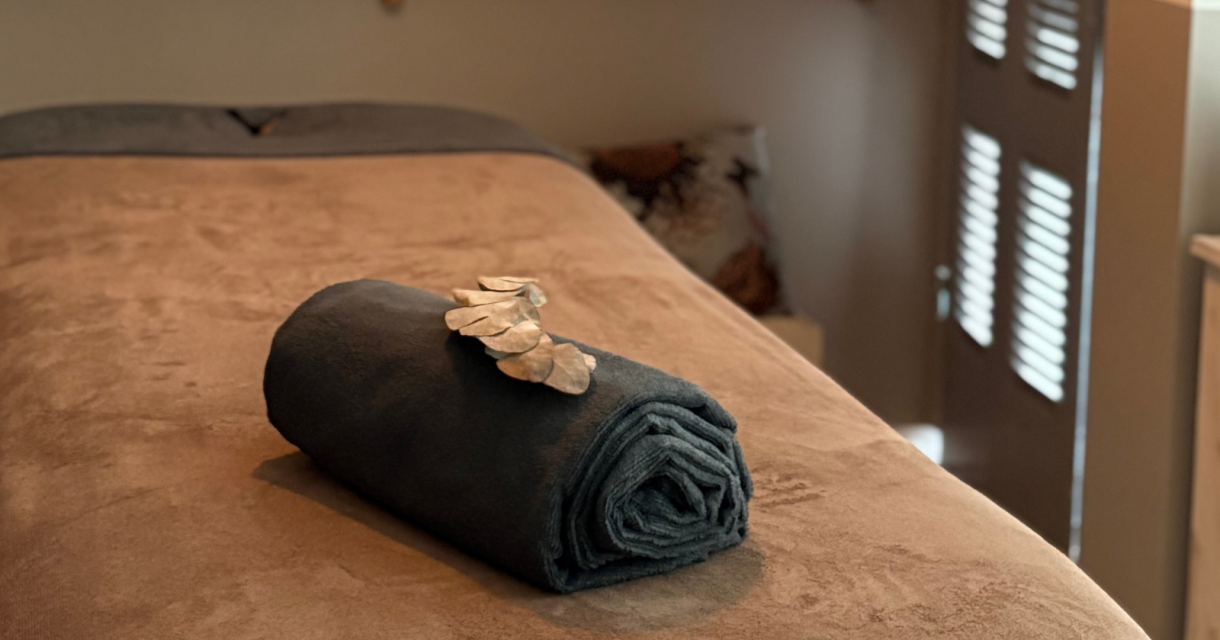 Massagekamer met opgerolde handdoek en edelstenen op een behandeltafel, gedimd licht en rustgevende sfeer