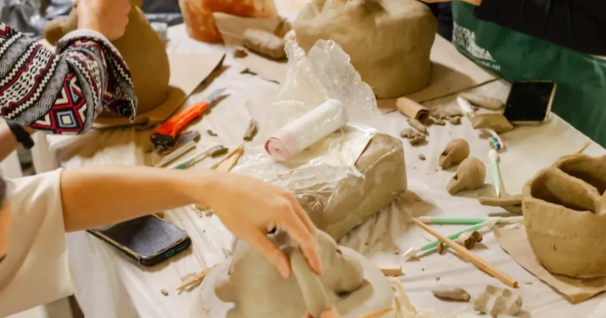 Deelnemers vormen kleien beelden aan een tafel.