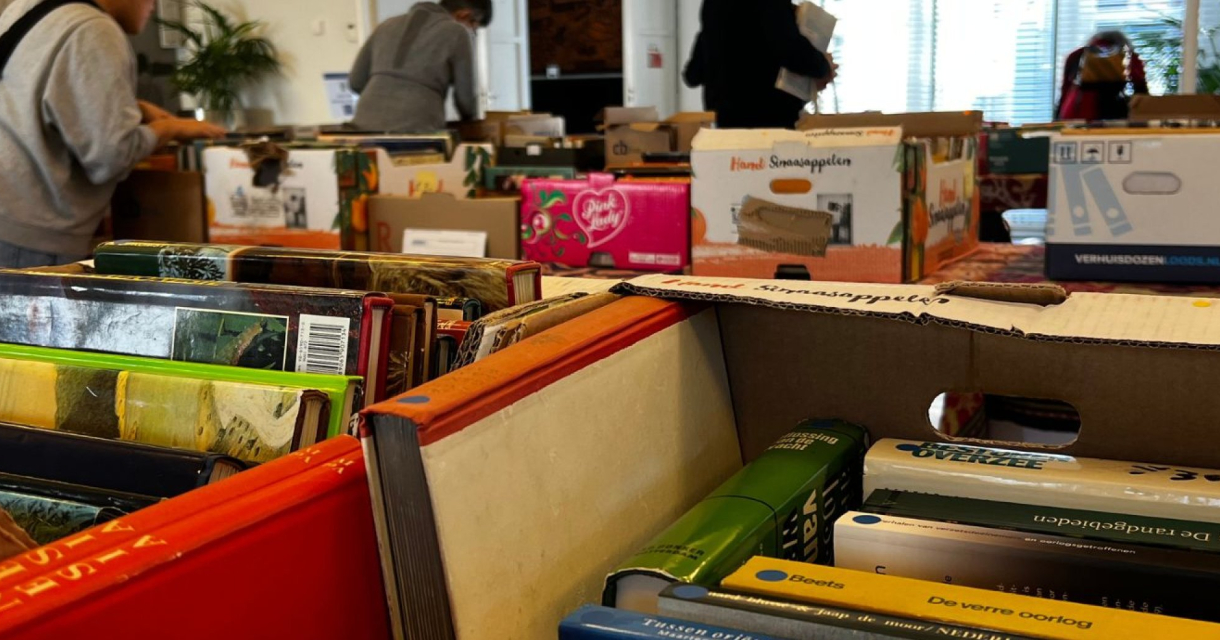 Mensen kijken naar dozen met boeken tijdens een boekenmarkt.