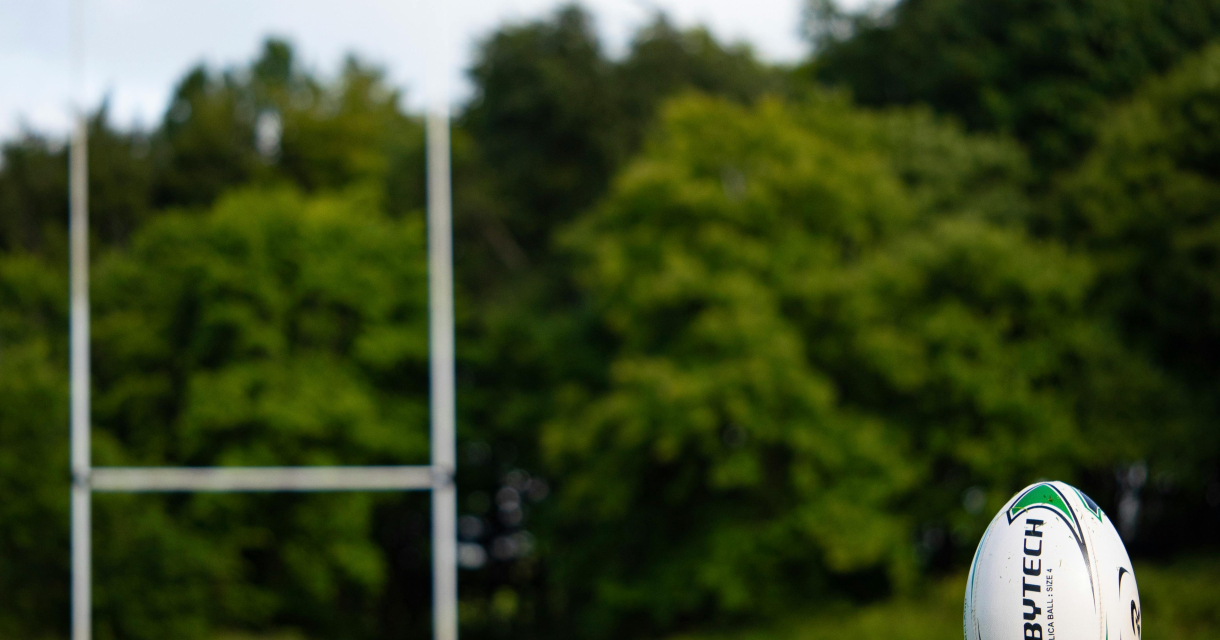 Een rugbybal ligt op een groen veld met goalposts.