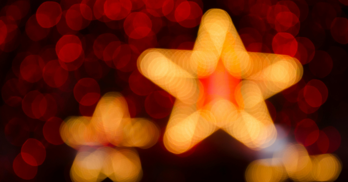 Vage gouden kerststerren met rode achtergrond en lichtbollen in bokeh-effect