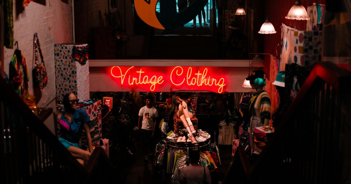 Trapafgang naar een kleurrijke vintagewinkel met neonbord en etalagepoppen in retrokleding
