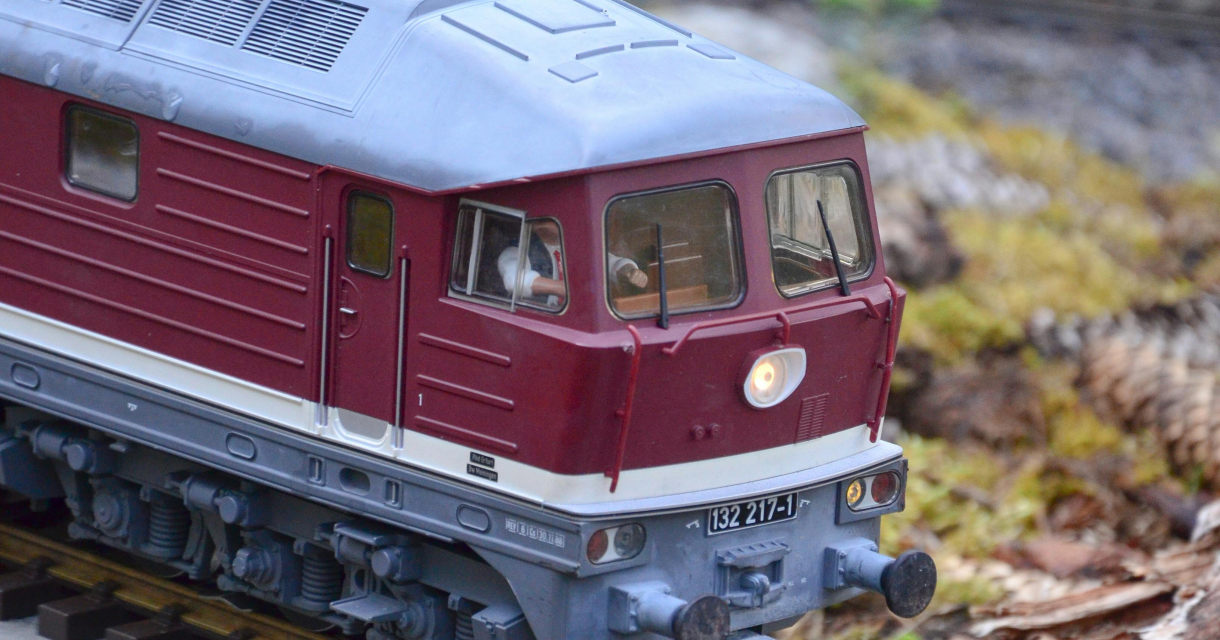 Rode modeltrein rijdt over een spoorlijn in een groen landschap.