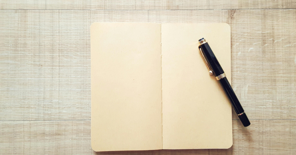 Een leeg notitieboek ligt open naast een zwarte pen.