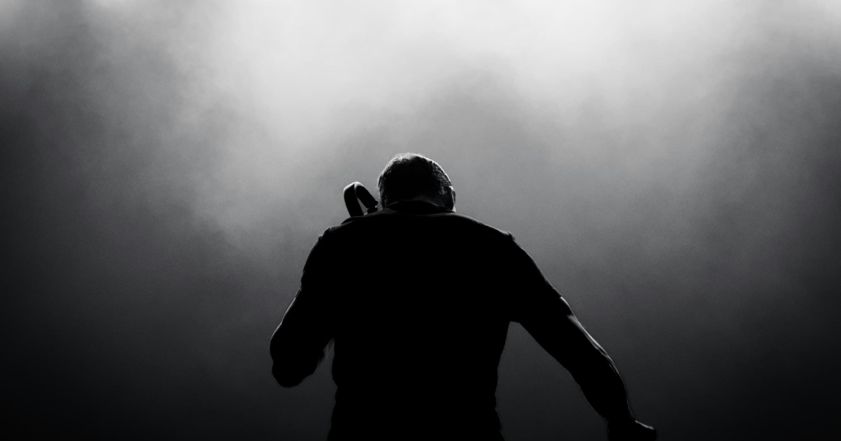 Een DJ is te zien van achteren, met verlichting en rook op het podium.