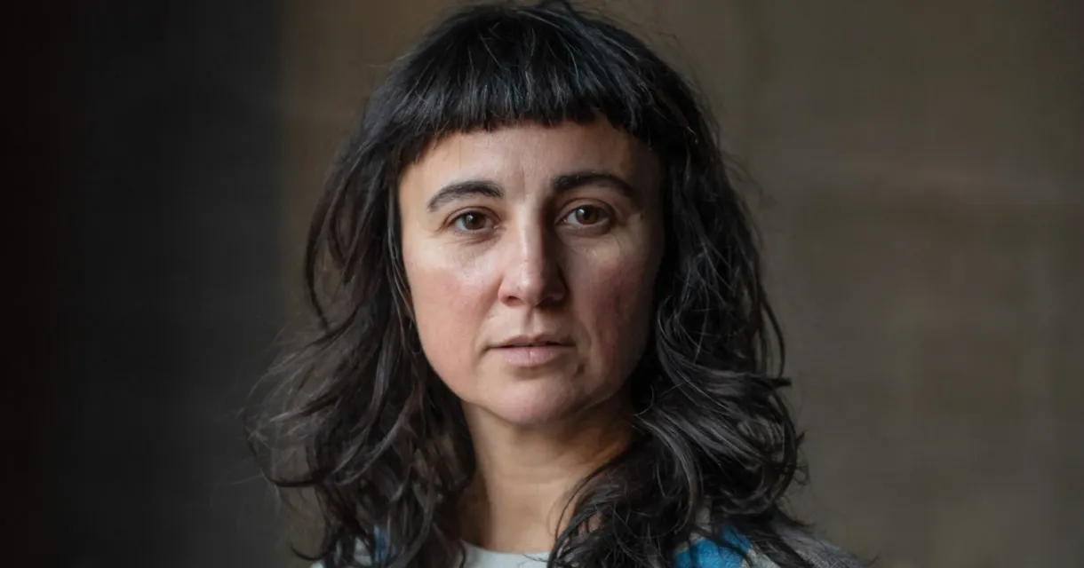 Een vrouw met krullend haar kijkt recht in de camera.