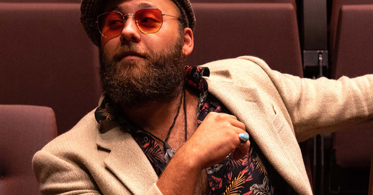 Een man met een baard en hoed zit ontspannen in een theaterstoel.