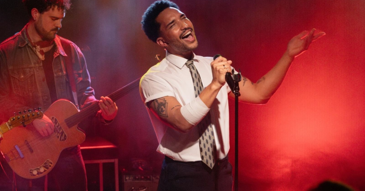 Zanger met microfoon en gitarist op podium in rood en geel licht tijdens liveoptreden