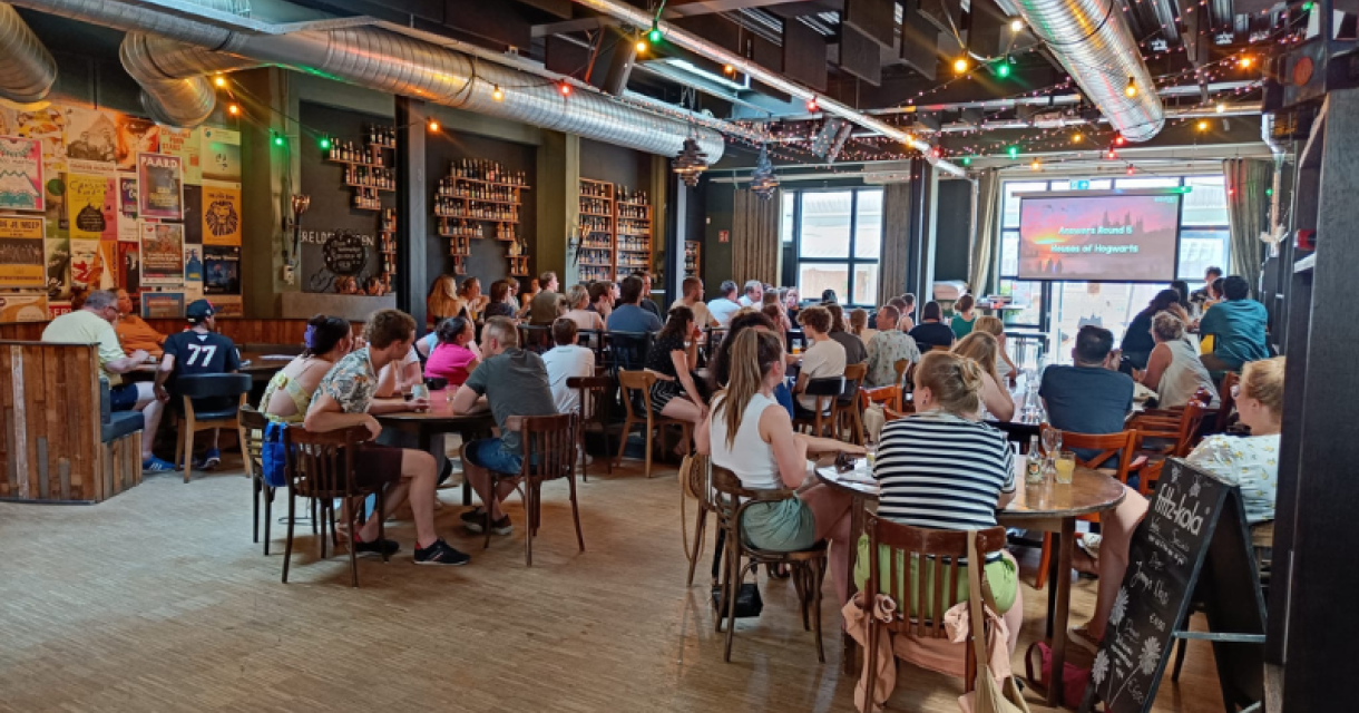 Mensen zitten aan tafels in een café met een presentatie op de achtergrond.