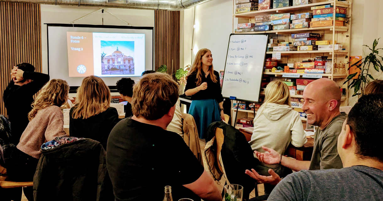 Een groep mensen kijkt naar een presentator tijdens een quizavond.
