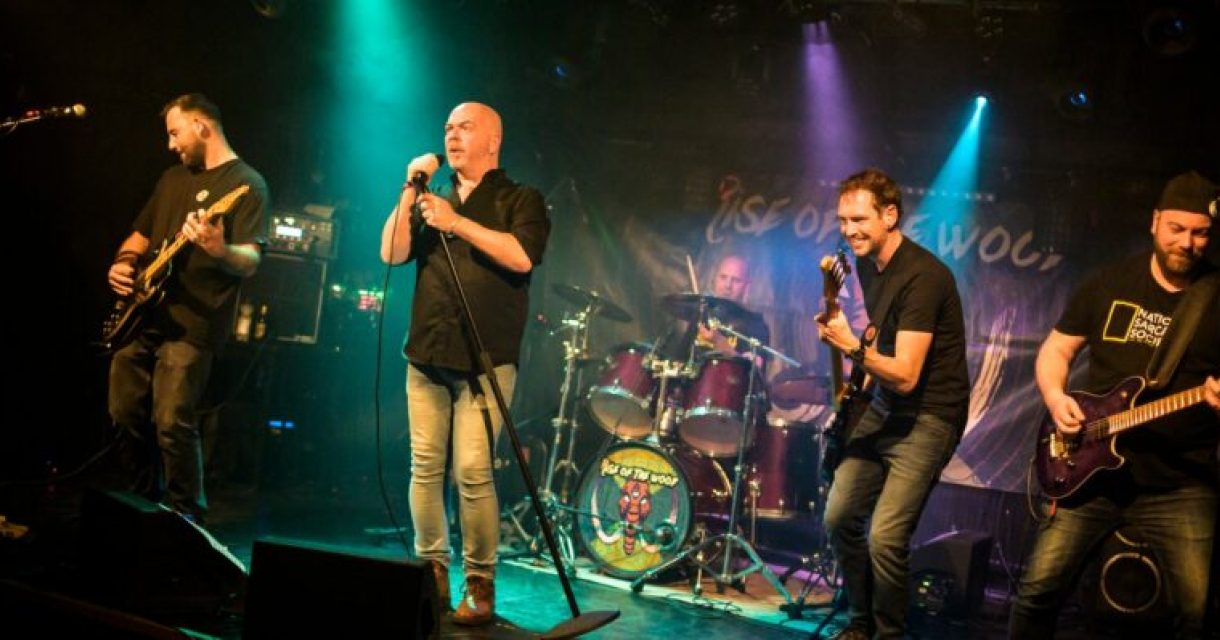 Bandoptreden op het podium. Vijf bandleden spelen live op een donker podium met kleurrijke lichten.