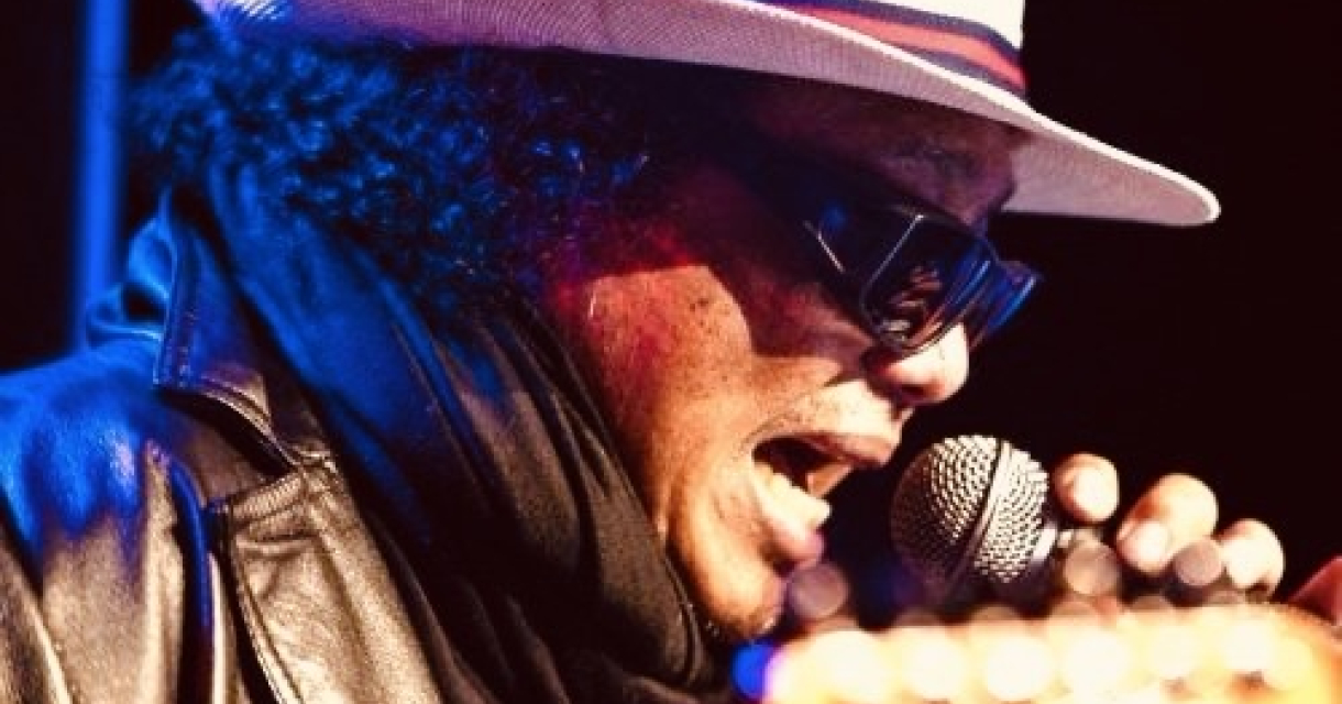 Man zingt in een microfoon terwijl hij een gitaar vasthoudt.