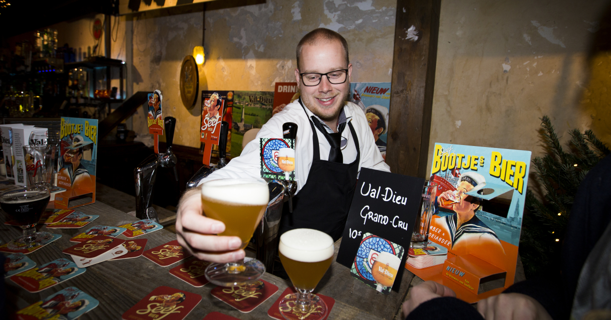 Barman met bril schenkt blond bier in op een sfeervol ingericht speciaalbierfestival