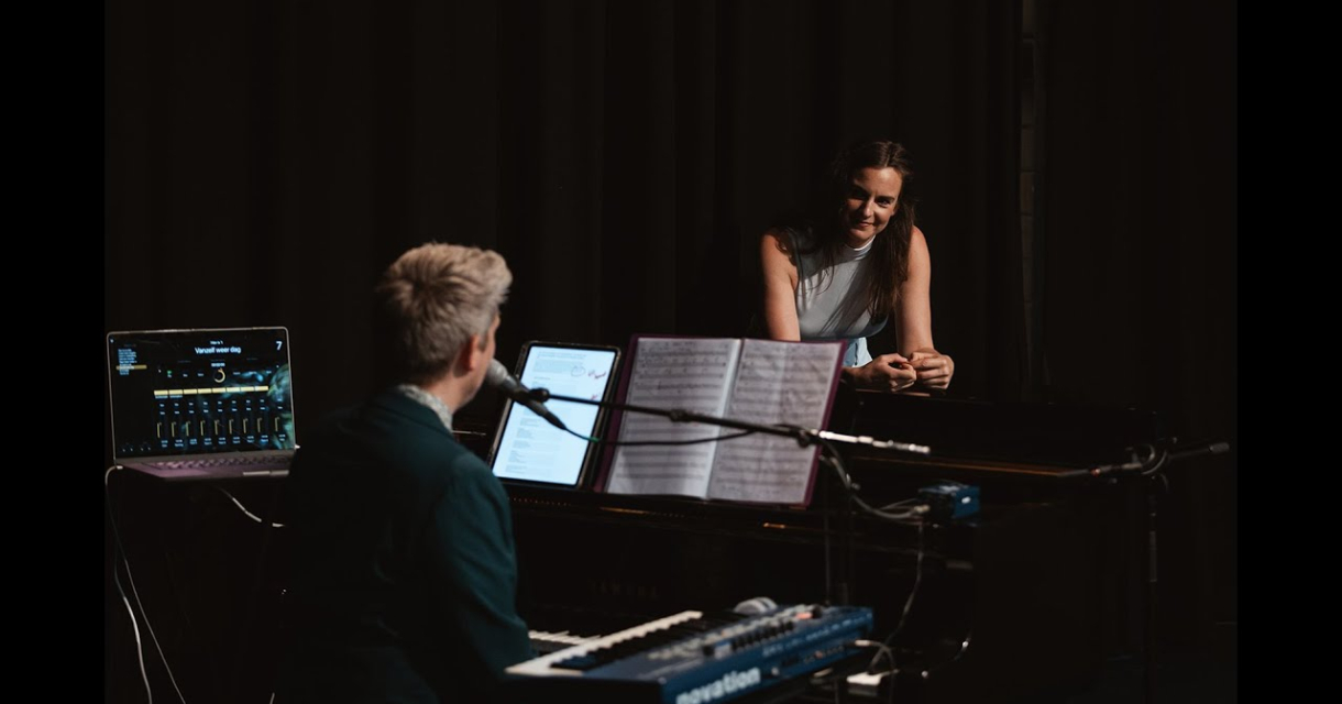 Een zangeres luistert naar de pianist tijdens een optreden.