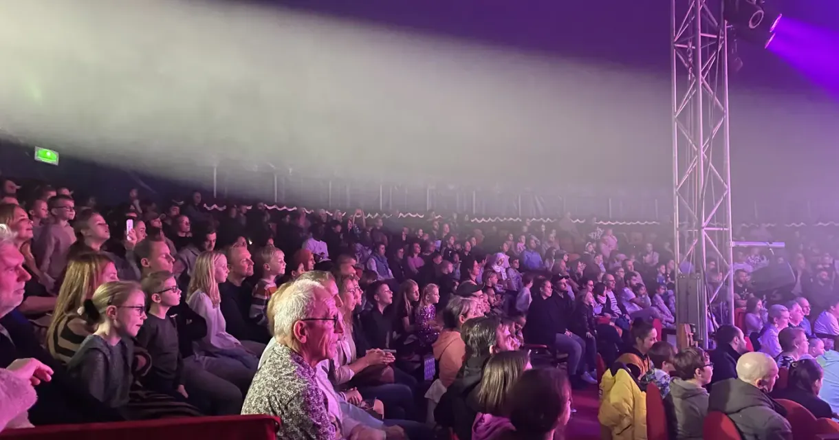 Een druk publiek in een theatertent met lichteffecten