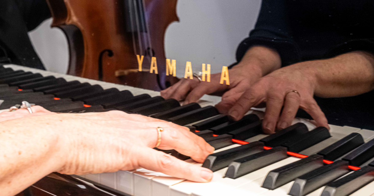 Twee handen pianaspelend gespiegeld in een Yamaha piano