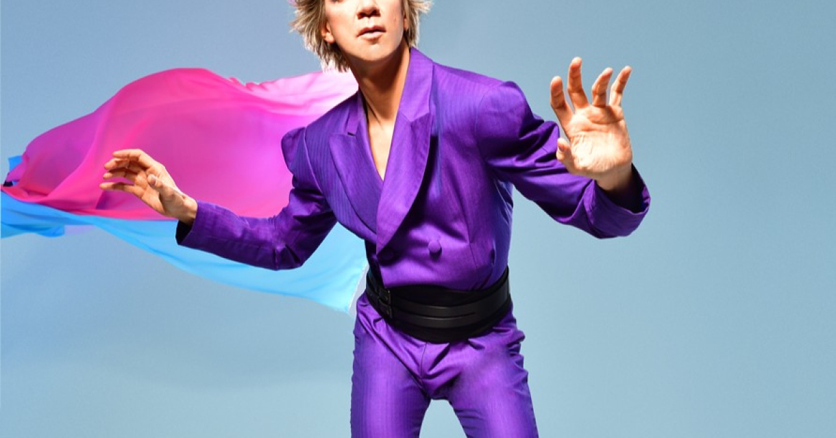 Een persoon in een paarse outfit met een roze en blauwe cape, poserende met een dynamische houding.