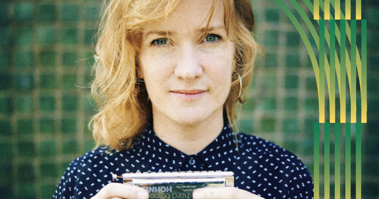Een vrouw met blond haar houdt een mondharmonica vast.