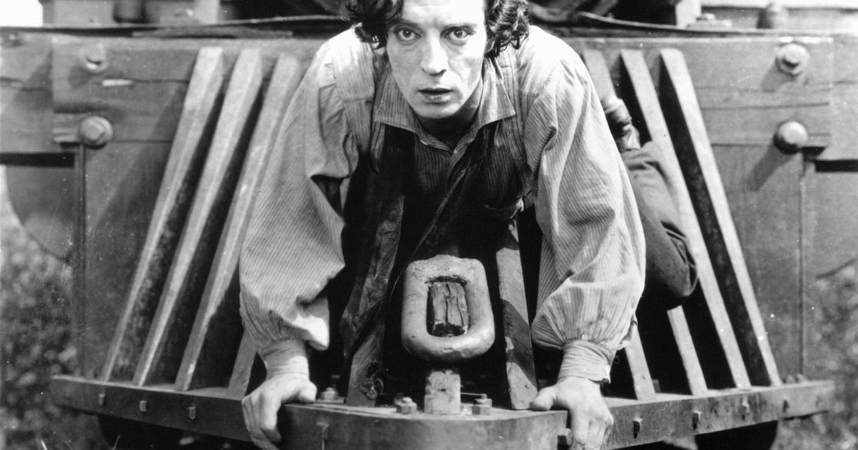 Zwart Wit foto van acteur Buster keaton op de locomotief van een trein. 