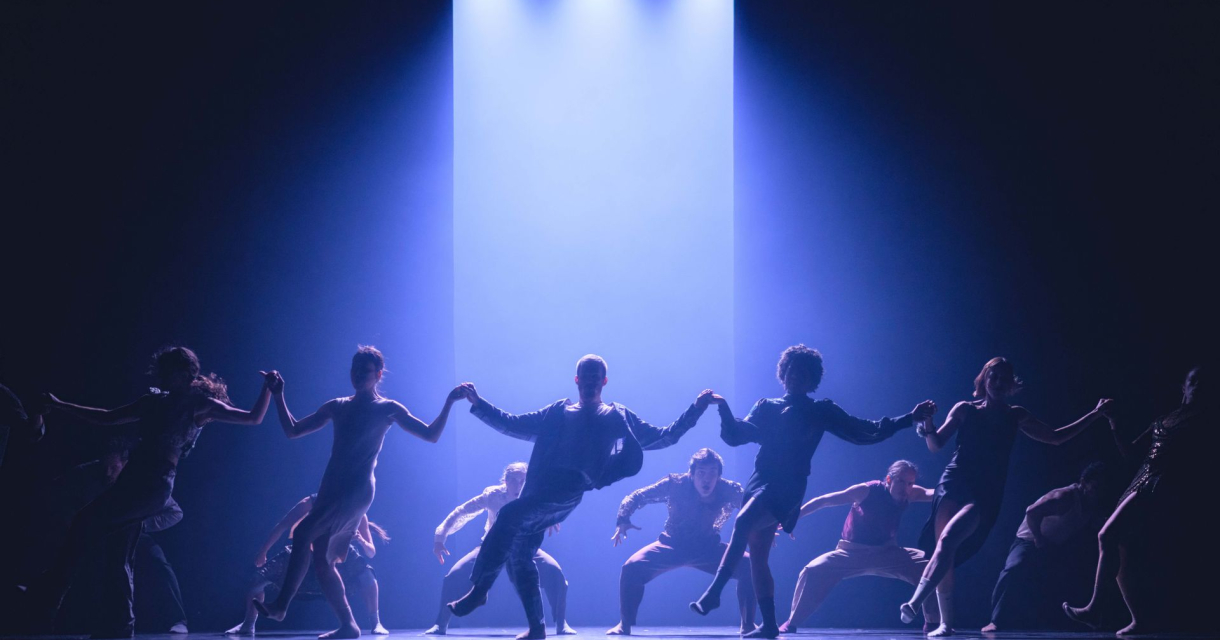 Silhouetten van dansers van Theatre of dreams die hand in hand in een kring dansen op een blauw verlicht podium