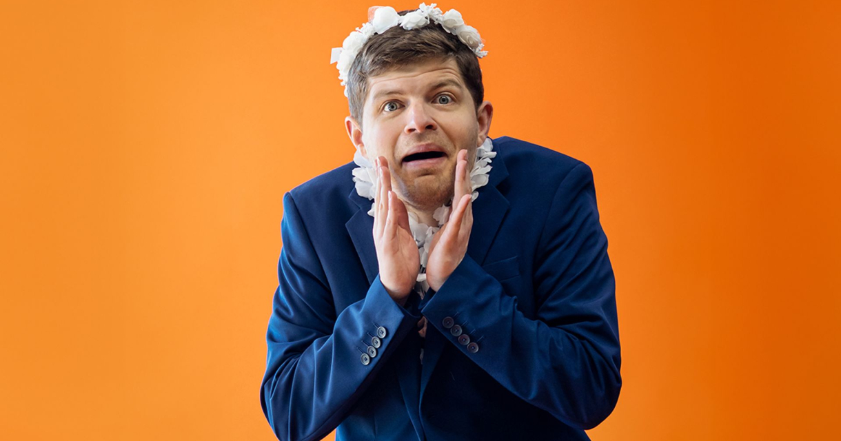 Man in een blazer met bloemenkrans en een verraste uitdrukking