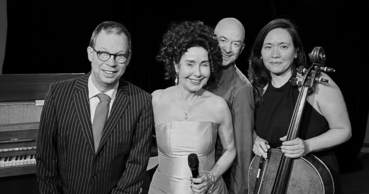 Een vrouwelijke zangeres met een microfoon en drie muzikanten.