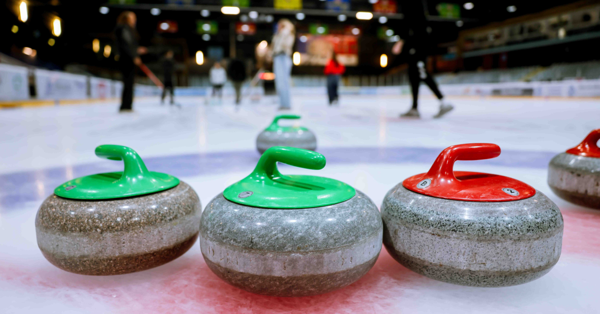 Curlingstenen met groene en rode handgrepen op een ijsbaan, mensen spelen op de achtergrond