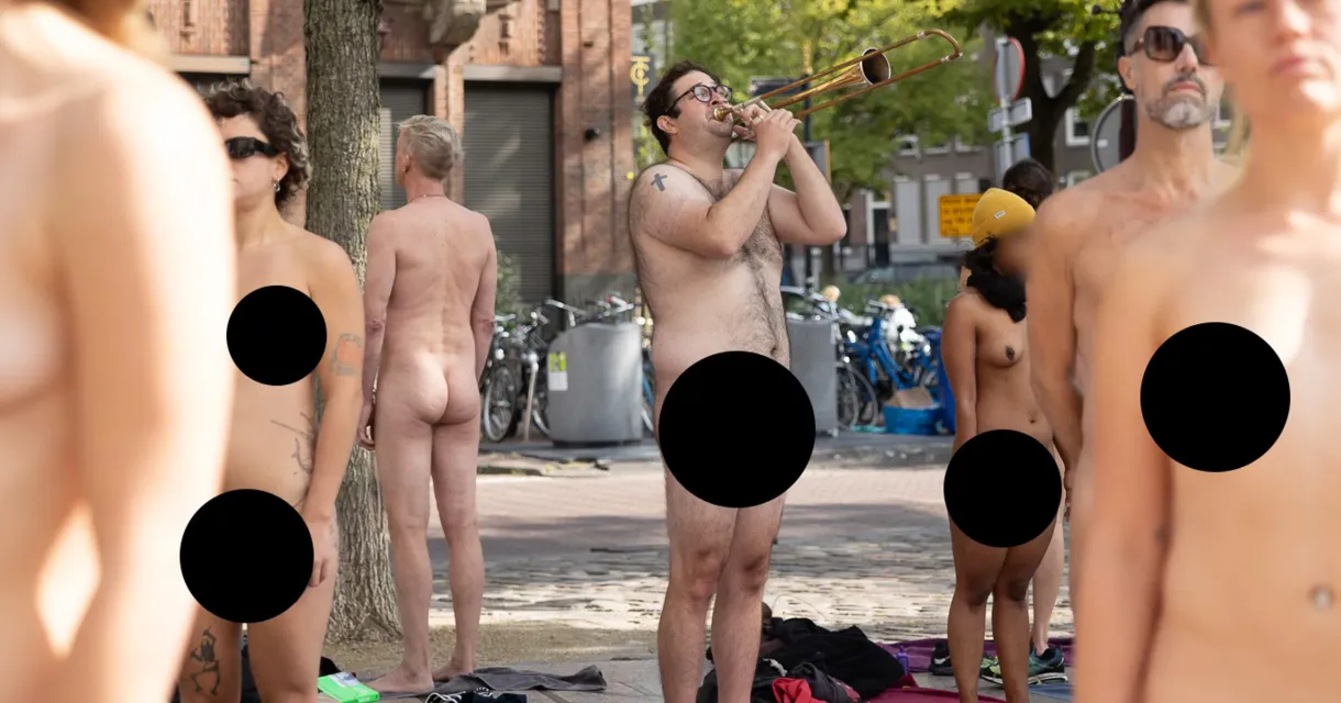 Een groep mensen in de stad, enkele naakt, terwijl een man op een trombone speelt.