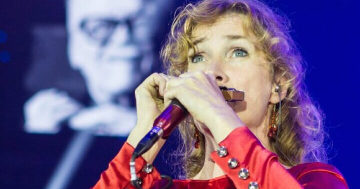 Zangeres in een rode jurk met een mondharmonica op het podium.