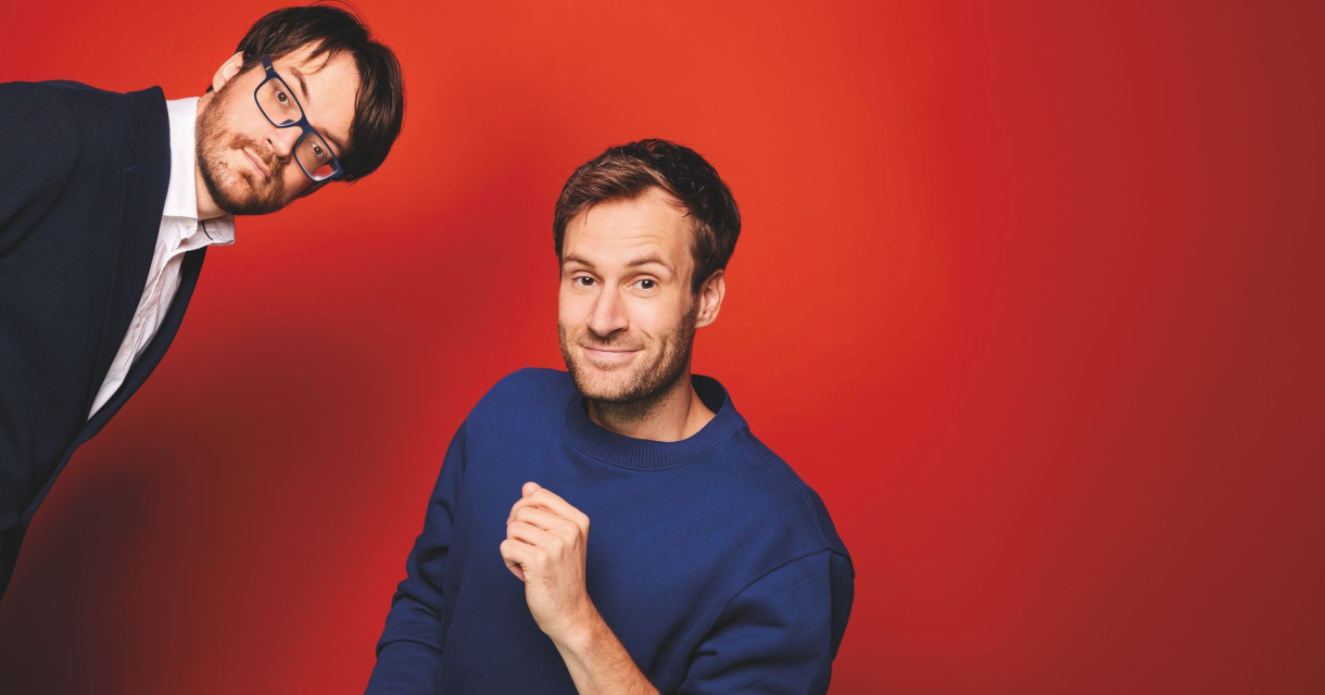 Twee mannen poseren voor een rode achtergrond.