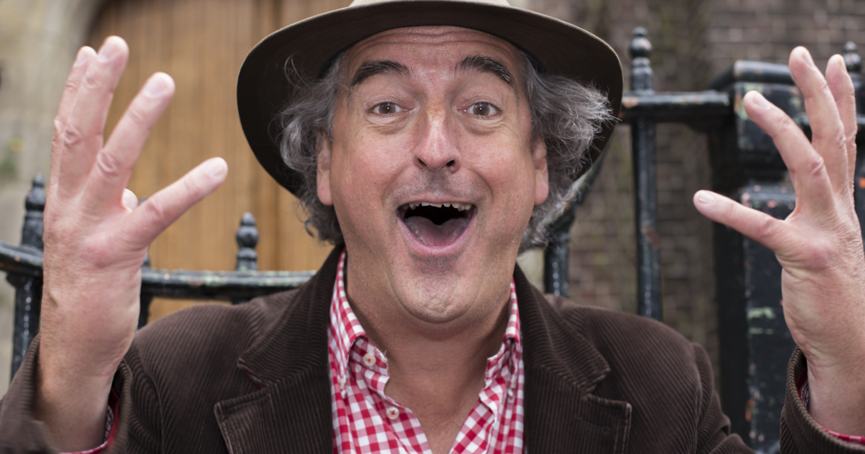 Portretfoto van verteller-Franciscus van Storytrail. Hij heeft een hoedje op en kijkt vrolijk lachend de camera in met zijn handen omhoog alsof hij iets uitlegt. 