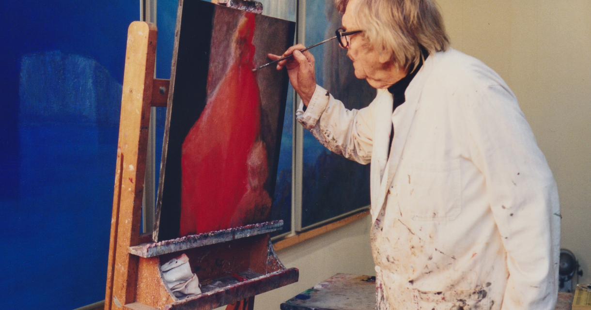 Kunstenaar in witte jas schildert op een ezel in een atelier, omringd door blauwe doeken aan de muur Kunstenaar in witte jas schildert op een ezel in een atelier, omringd door blauwe doeken aan de muur