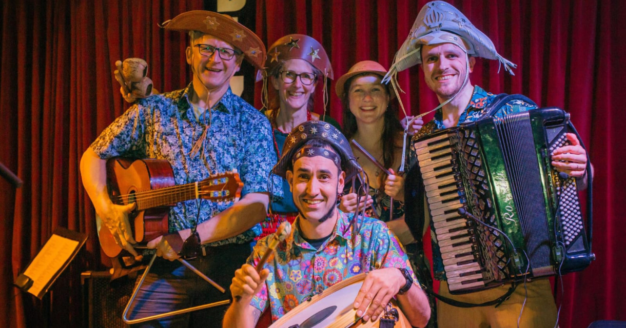 Groep muzikanten met hoedjes en diverse instrumenten op een podium