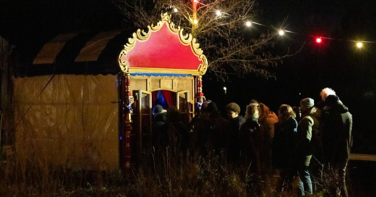 Mensen wachten in de nacht bij een kleurrijk poppentheater.