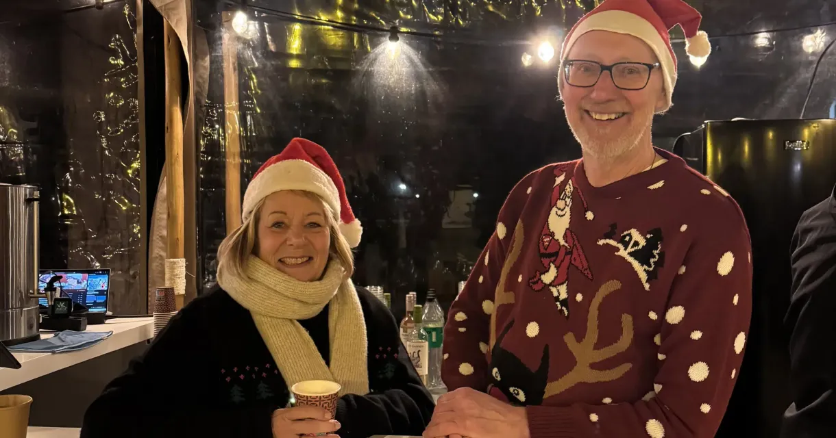 Twee mensen in kersthoeden en mutsen staan achter een bar.