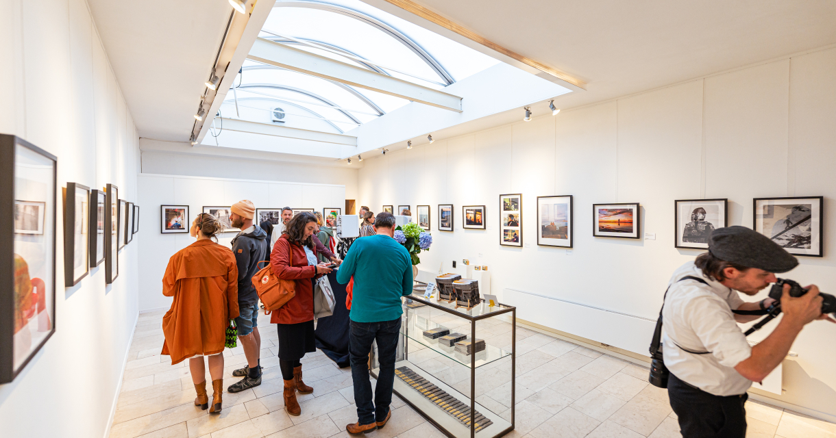Bezoekers bekijken foto's in een galerie met witgekleurde muren.