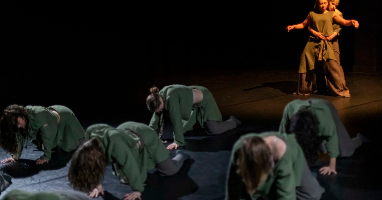 Groep dansers in groene outfits performen op het podium.