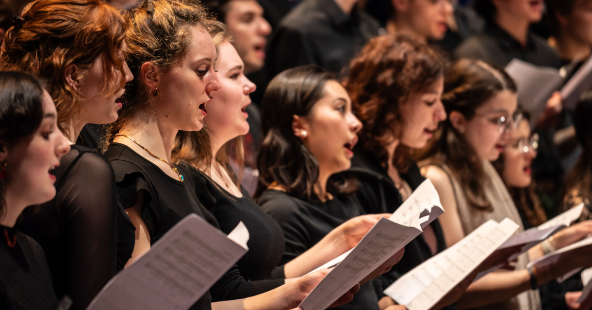 Een groep mensen zingt samen en houdt bladmuziek vast.