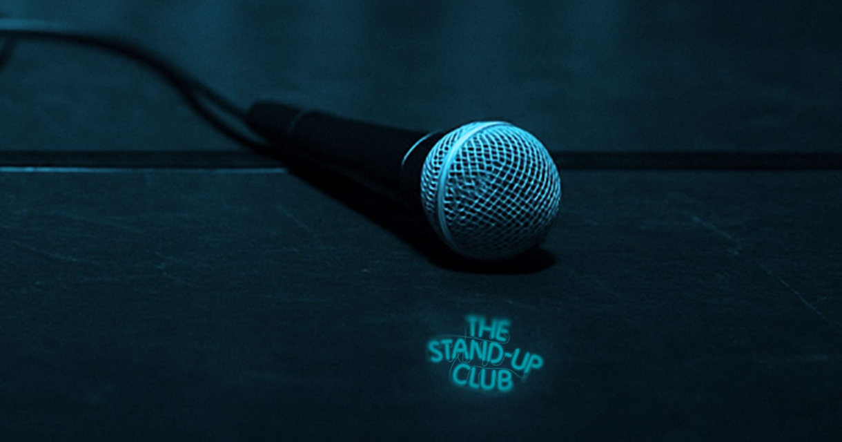Microfoon liggend op een podium met de tekst: the stand-up club Microfoon liggend op een podium met de tekst: the stand-up club