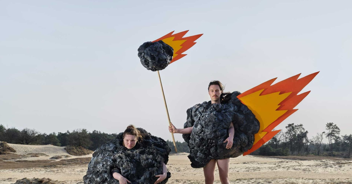 Twee personen verkleed als vurige meteorieten in zanderig duinlandschap met blauwe lucht Twee personen verkleed als vurige meteorieten in zanderig duinlandschap met blauwe lucht