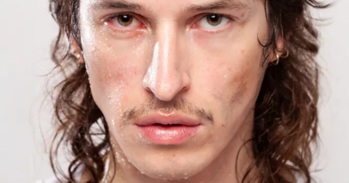 Close-up van een man met nat gezicht, lange donkere krullen en een dun snorretje, die intens in de camera kijkt. Close-up van een man met nat gezicht, lange donkere krullen en een dun snorretje, die intens in de camera kijkt.