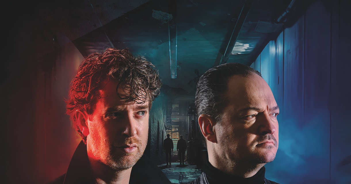 Twee mannen met serieuze gezichten staan in een donker, mysterieus verlicht gangpad; de ene belicht met rood licht, de andere met blauw.